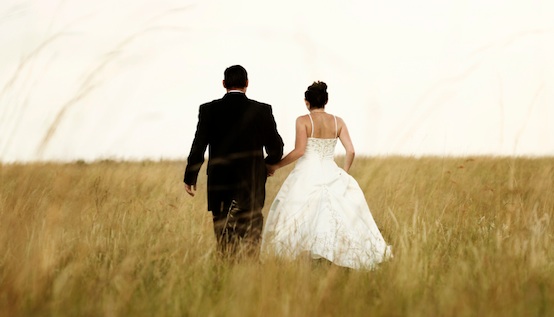 A newly wed couple walking through a grassland, holding hands